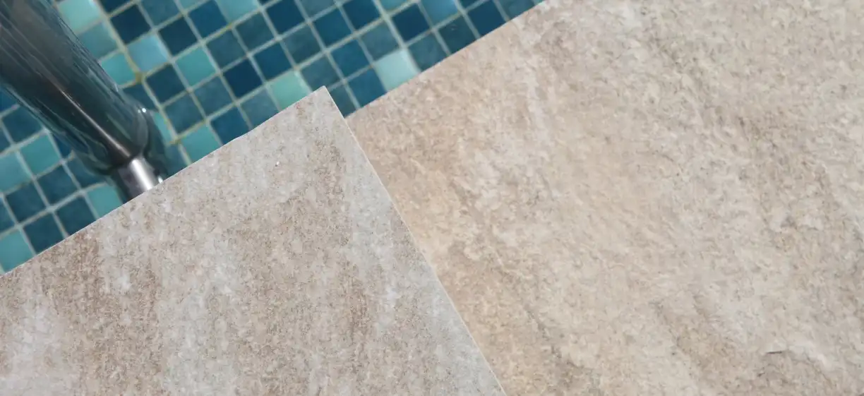 Light stone flooring at the edge of a pool with blue mosaic tiles